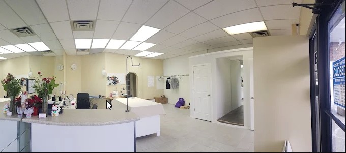 The reception counter inside New Stitch Tailor, fresh flowers, a work table and the doorway to the workshop
